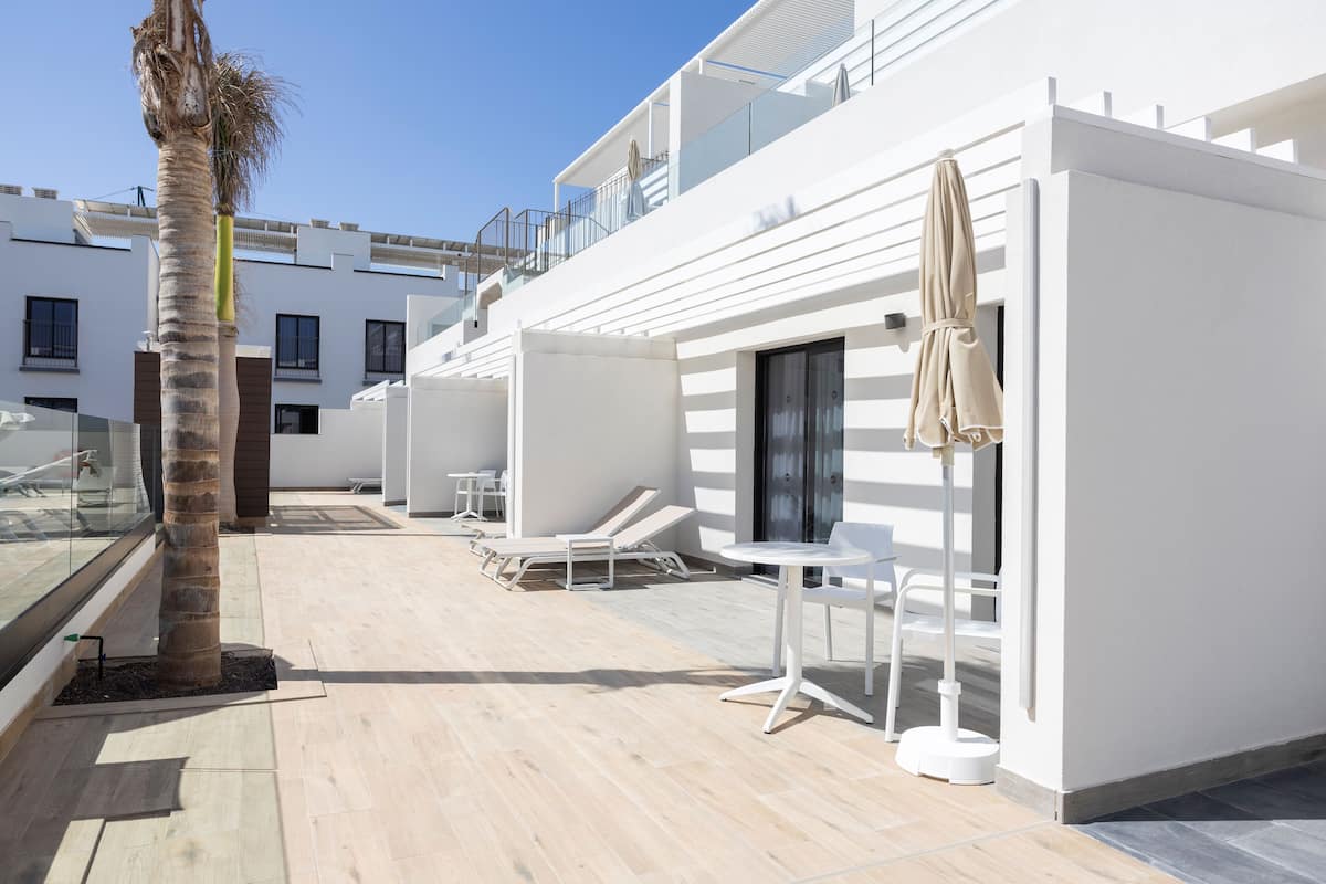 A modern outdoor lounge area with white furniture, a palm tree, and a clear blue sky.