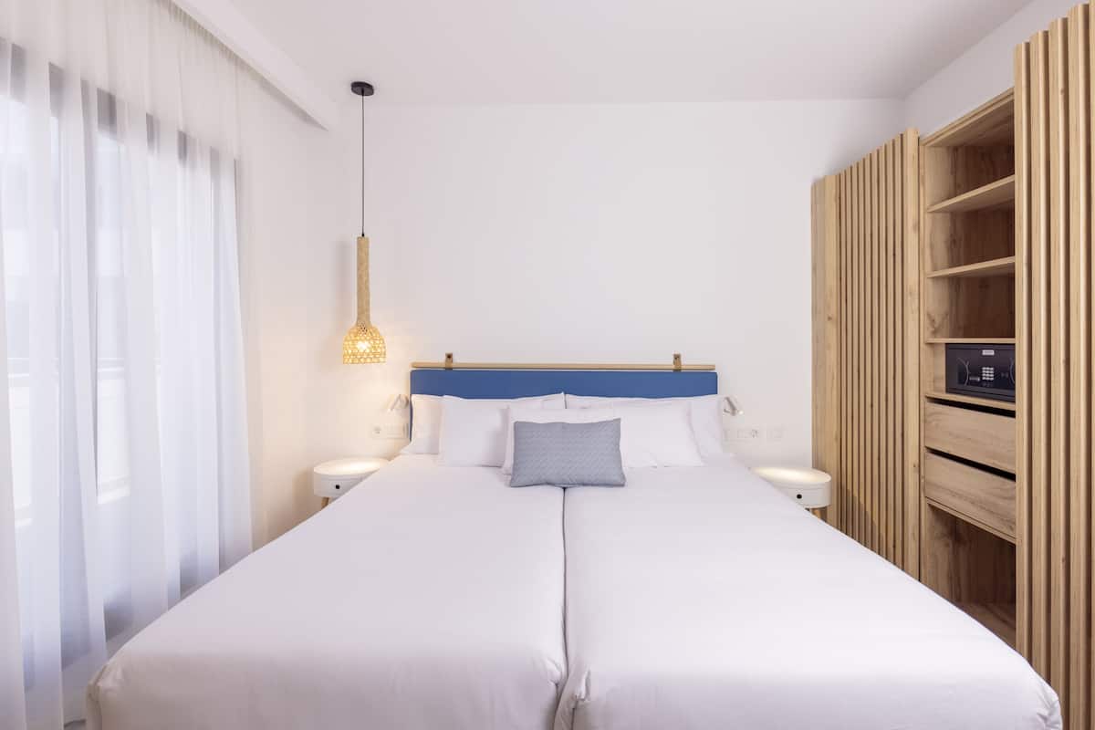 A double bed with white linens, a blue headboard, and a bedside table with a lamp.
