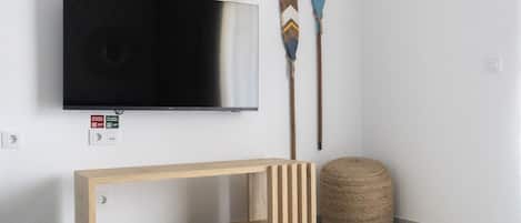 Ein modernes Wohnzimmer mit einem an der Wand befestigten Flachbildfernseher, einem Holzkonsolentisch, zwei dekorativen Schlägern und einem gewebten Hocker.