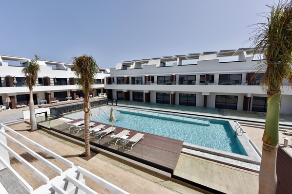 A rooftop pool area with multiple lounge chairs and palm trees. - Esmeralda Cotillo Homes by LIVVO (La Oliva)