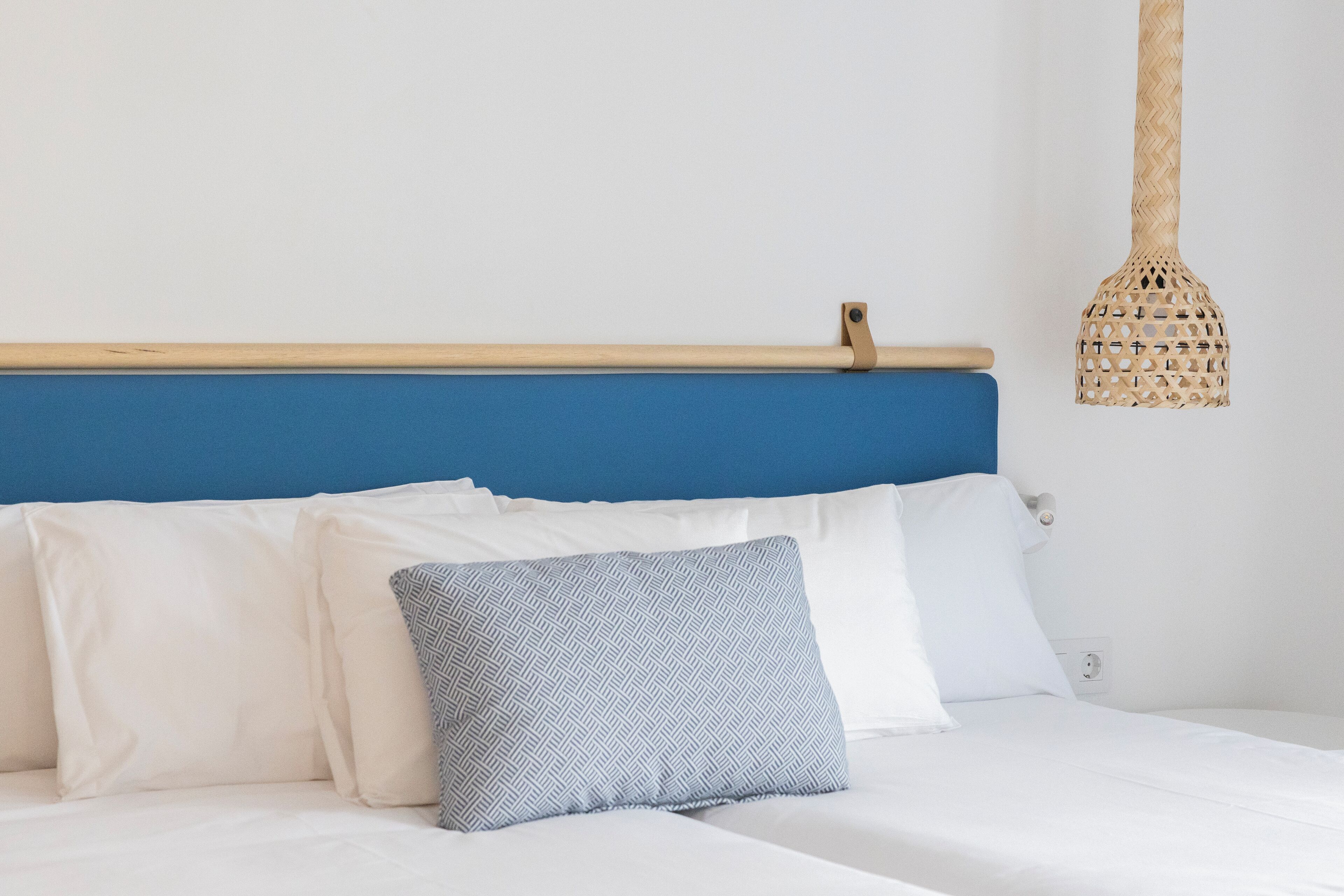 Una cama con almohadillas blancas y azules, un cabecero azul y una lámpara de techo de fibras.
