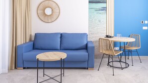 A room with a blue sofa, a round wooden table, wicker chairs, a wall-mounted mirror, and a view of the ocean through a window. - Esmeralda Cotillo Homes by LIVVO (La Oliva)