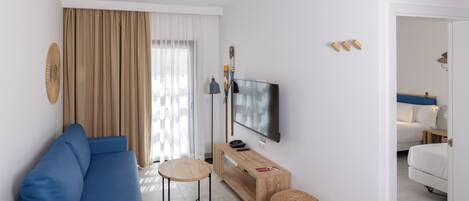 Een moderne woonkamer met een blauwe bank, een houten salontafel, een televisie en een groot raam met gordijnen.