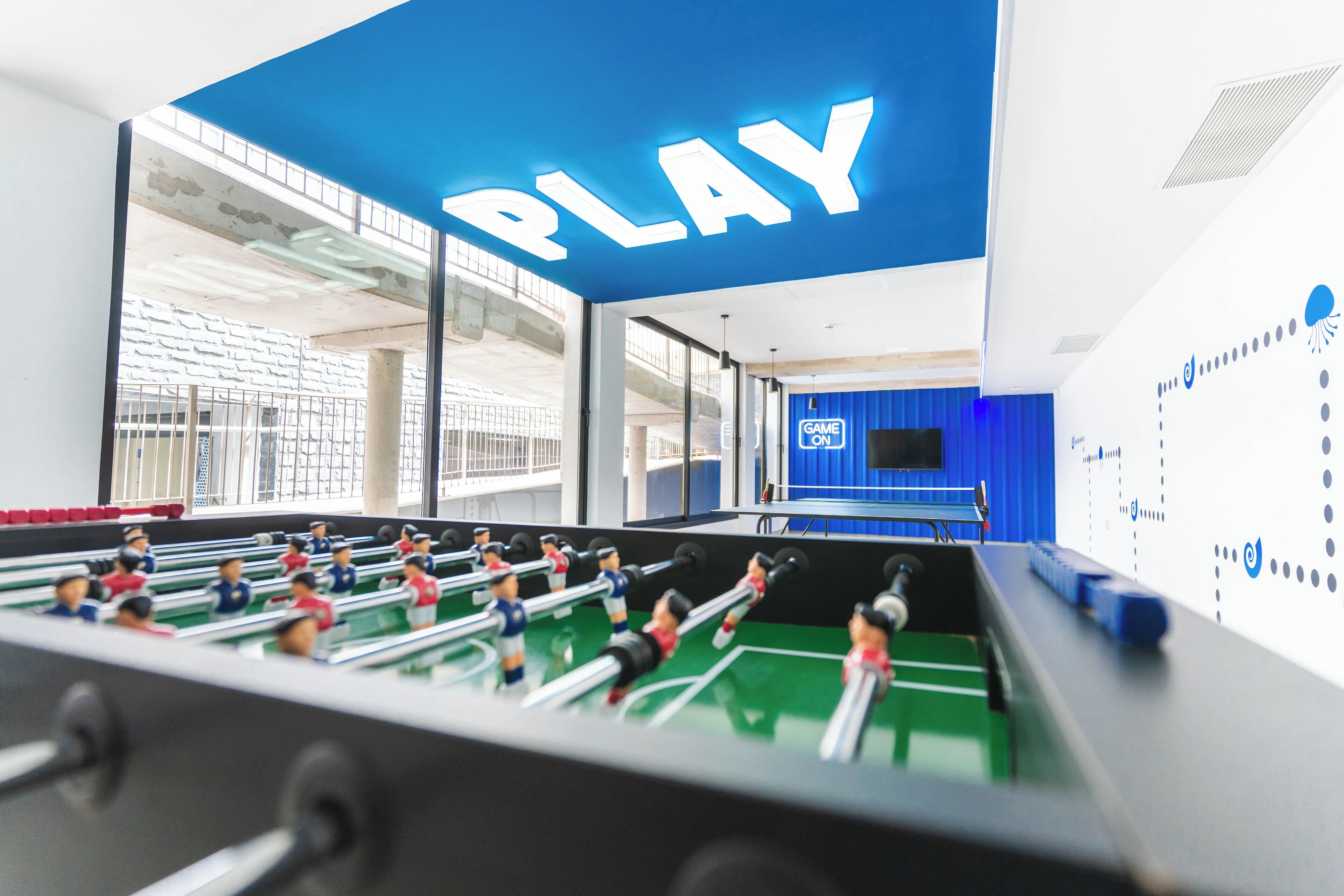 A foosball table in a brightly lit room with a large 'PLAY' sign on the wall.