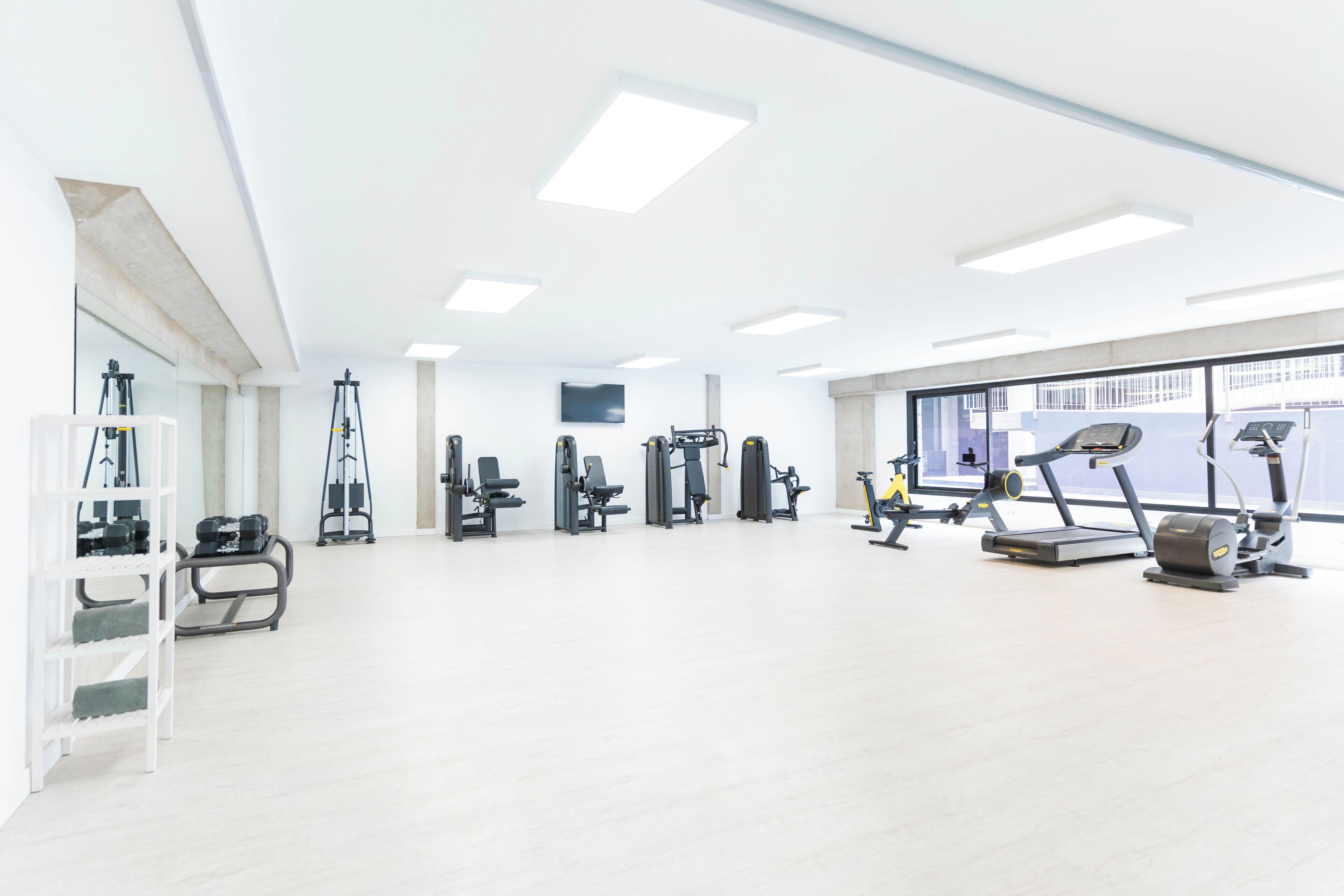 A spacious gym with various exercise equipment, a large window providing natural light, and a clean, modern design.