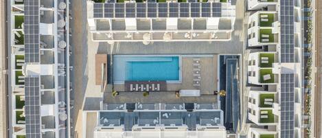 An aerial view of a modern hotel with a central swimming pool, multiple balconies, and solar panels.