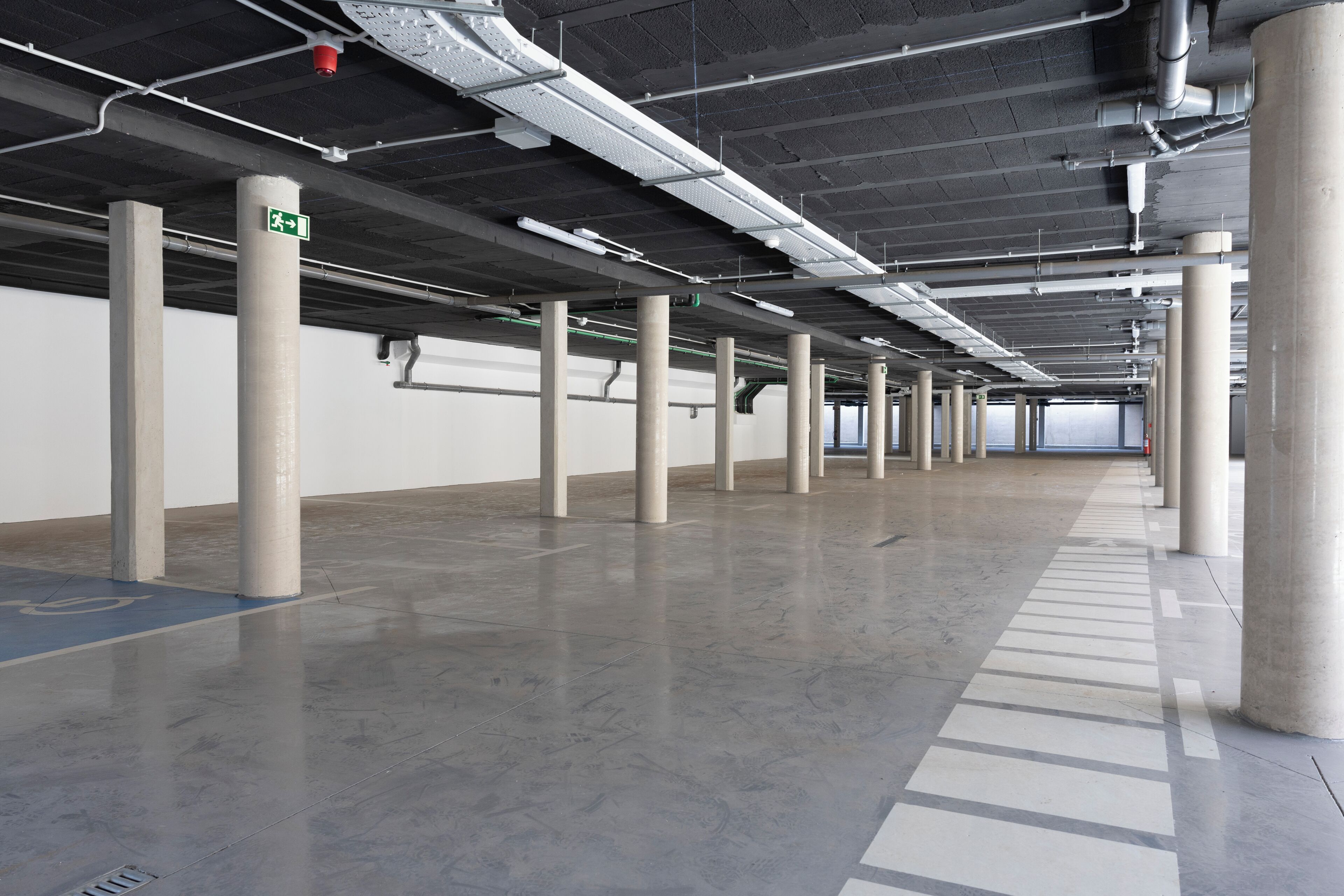 A spacious parking garage with concrete pillars, clear ceiling pipes, and a clean, reflective floor.