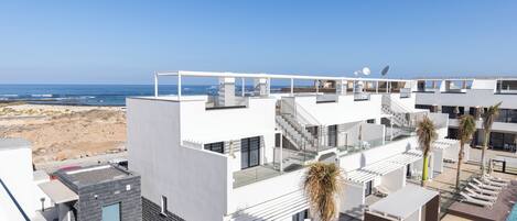 A modern hotel with a rooftop pool, multiple balconies, and a view of the beach.