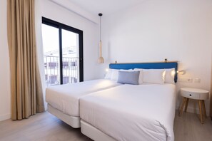 A hotel room with two beds, a large window with curtains, a bedside table, and a hanging light fixture. - Esmeralda Cotillo Homes by LIVVO (La Oliva)