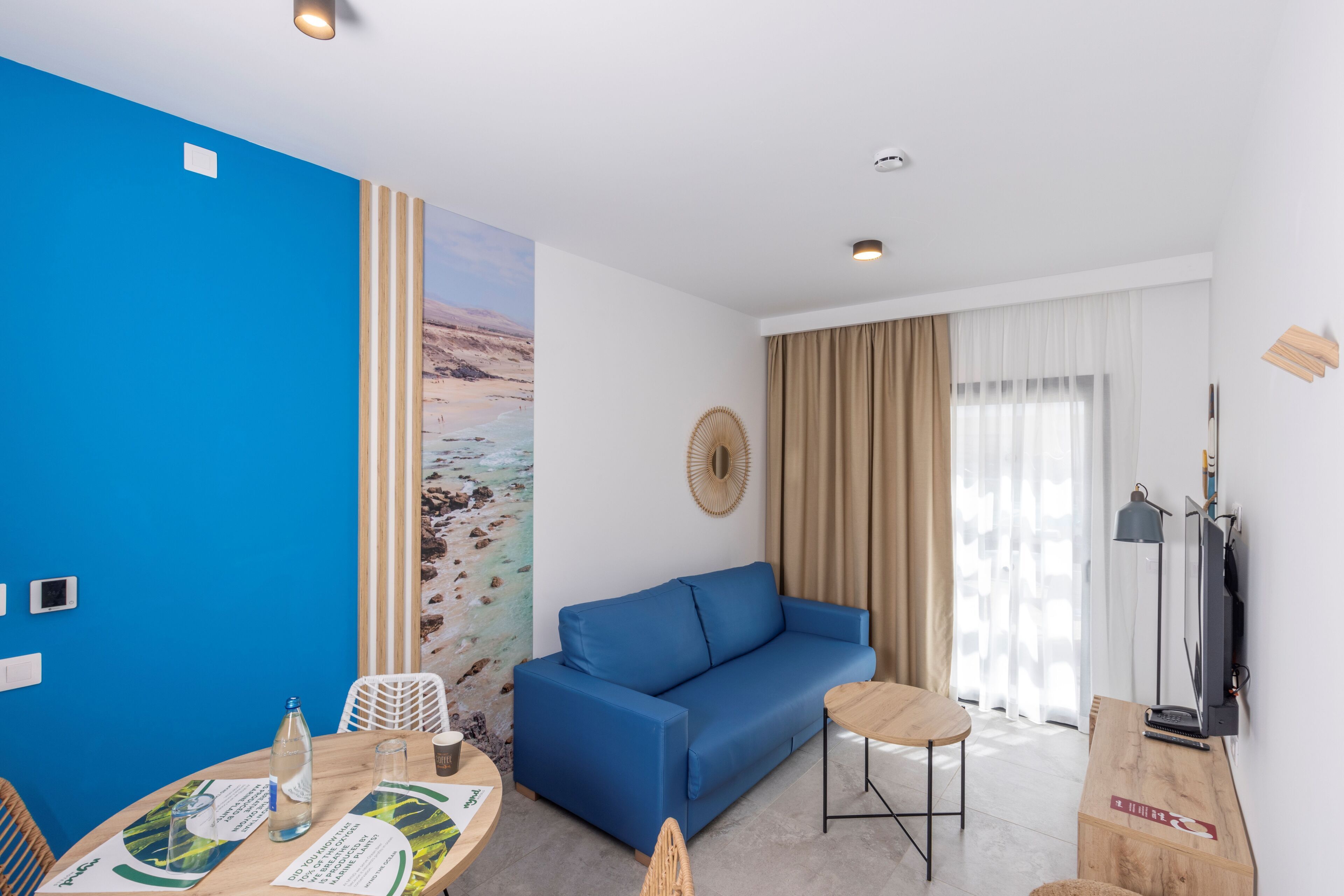 A modern living room with a blue sofa, a wooden coffee table, a TV, and a large window with curtains.