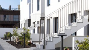 A modern building with a staircase leading to a balcony, surrounded by greenery and a paved walkway. - Esmeralda Cotillo Homes by LIVVO (La Oliva)