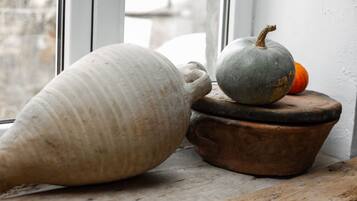 Un jarrón de cerámica grande y una pequeña calabaza sobre una mesa de madera rústica cerca de una ventana.