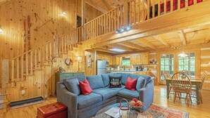 A wooden cabin interior with a living room, kitchen, and dining area.