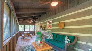 A cozy cabin interior with a wooden ceiling, a green sofa, a wooden table, and a wicker chair.