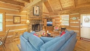 A cozy log cabin interior with a stone fireplace, a television, and a comfortable seating area.