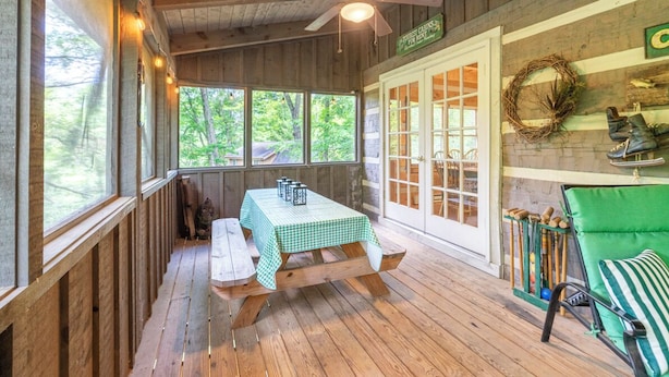 A wooden cabin with a table and benches, a ceiling fan, and a view of the outdoors.