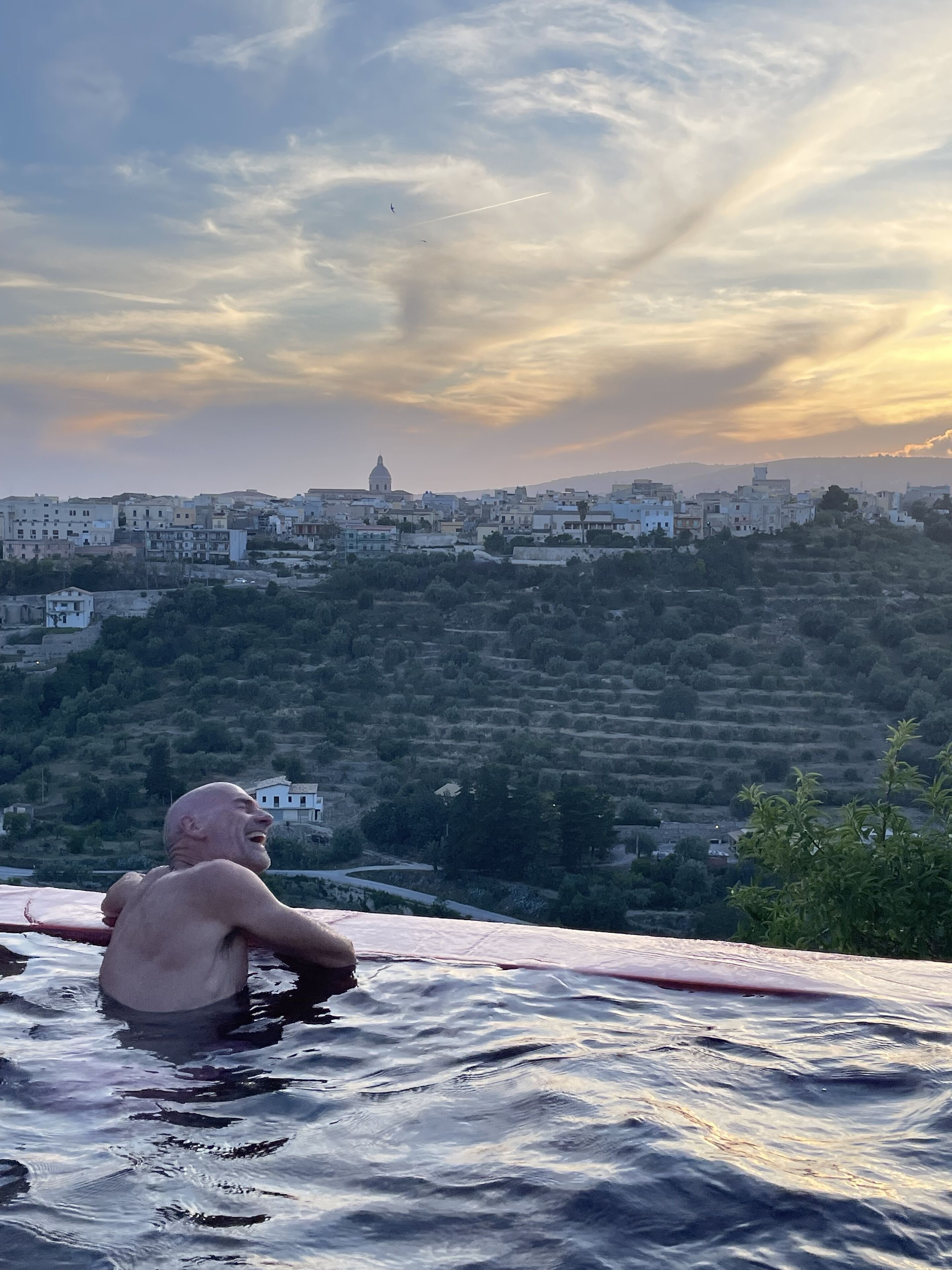 Ein Mann in einem Schwimmbecken mit Blick auf eine Stadt, Gebäude und Hügel.