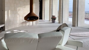 A modern interior with a white sofa, a hanging light fixture, and large windows.
