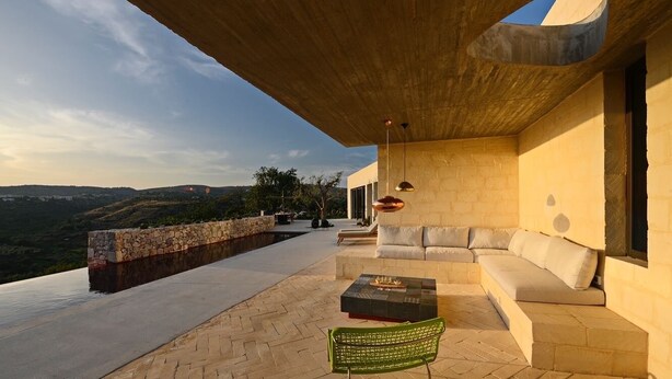 A modern outdoor seating area with a stone wall, a sofa, and a green chair.