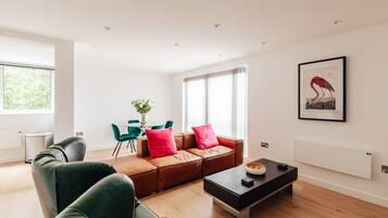 Ein modernes Wohnzimmer mit einer Ledersofa, grünen Sessel, einem Couchtisch und einem Essbereich mit Tisch und Stühlen.