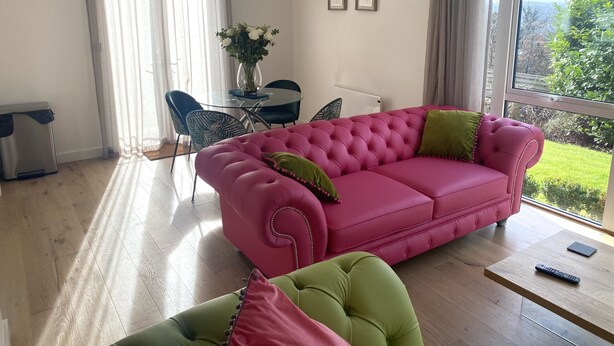 Un salón con sofá rosa, un sillón verde, una mesita y vistas a zonas verdes.