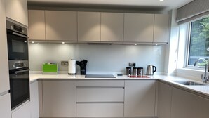 Una cocina moderna con armarios blancos, horno empotrado, cafetera de acero inoxidable y ventana con vistas a zonas verdes.