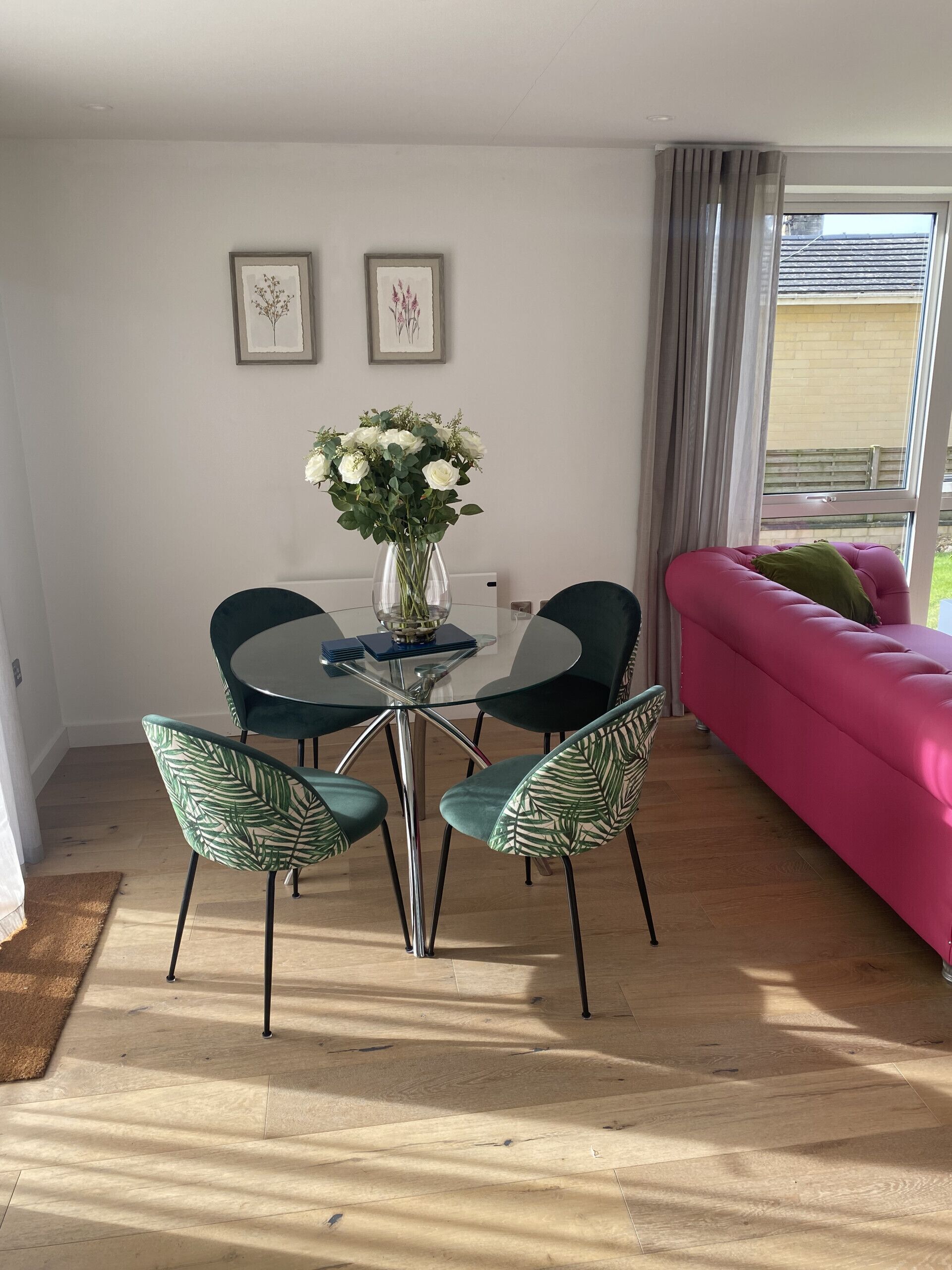 A dining area with a glass table and chairs, a vase with white flowers, and a pink sofa.