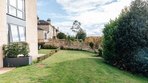 Une cour avec une pelouse, un mur en pierre et un bâtiment doté de grandes fenêtres.