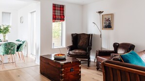 Un salon avec un fauteuil en cuir marron, une commode en bois et un fauteuil  à motifs verts.