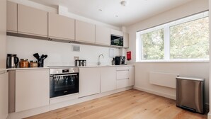 Eine moderne Küche mit weißen Schränken, einem Edelstahl-Kühlschrank und einem Fenster mit Blick auf Bäume.