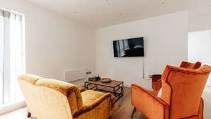 Ein modernes Wohnzimmer mit Sofa, Sesseln und Couchtisch. Ein Flachbildfernseher ist an der Wand angebracht.