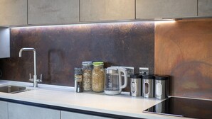 A modern kitchen with a stainless steel sink, a kettle, and various containers on the countertop.