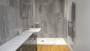A modern bathroom with a glass shower enclosure, a double sink vanity, and a wooden floor.