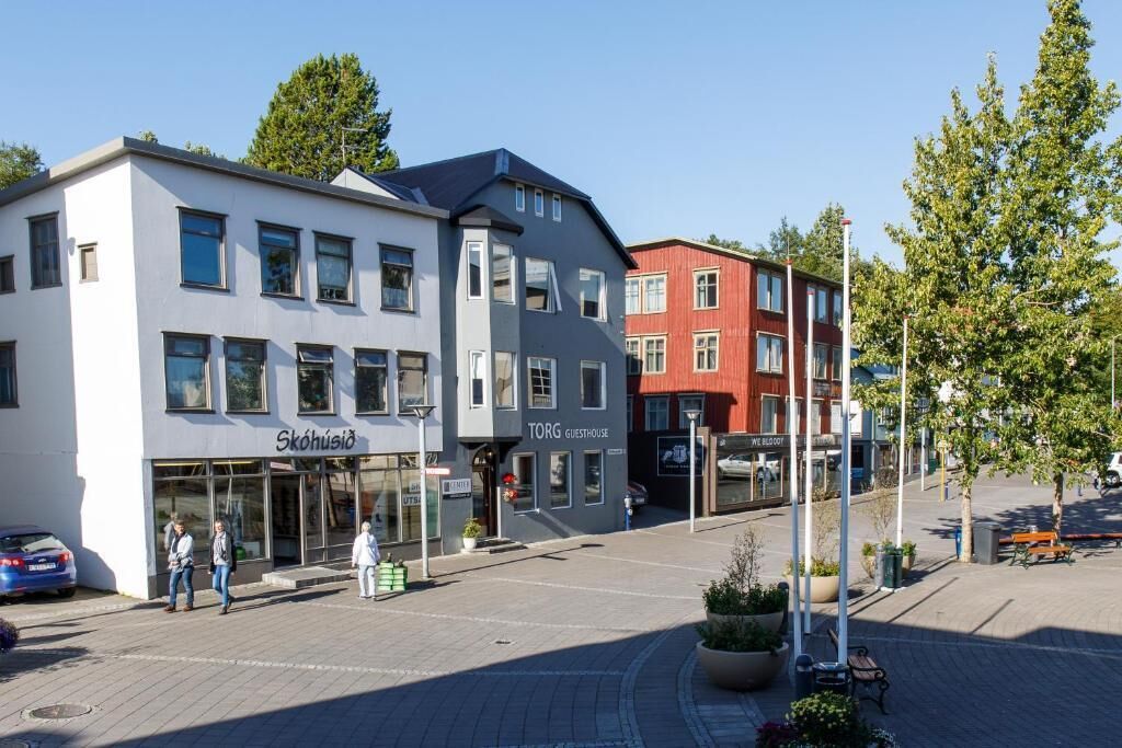 En moderne bygning med butiksvindue, der viser skiltene "Skohusied" og "Torg Guesthouse".