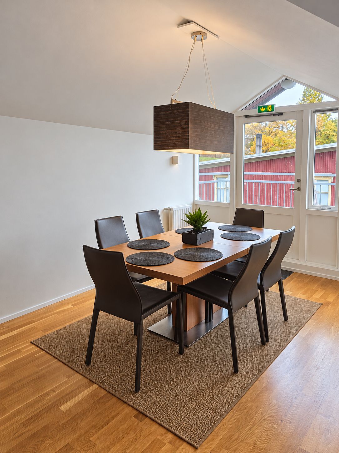A dining area with a wooden table, black chairs, and a hanging light fixture.