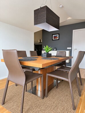 A modern dining area with a rectangular wooden table, six brown chairs, a potted plant, and a pendant light. - Torg Guest House (Akureyri)