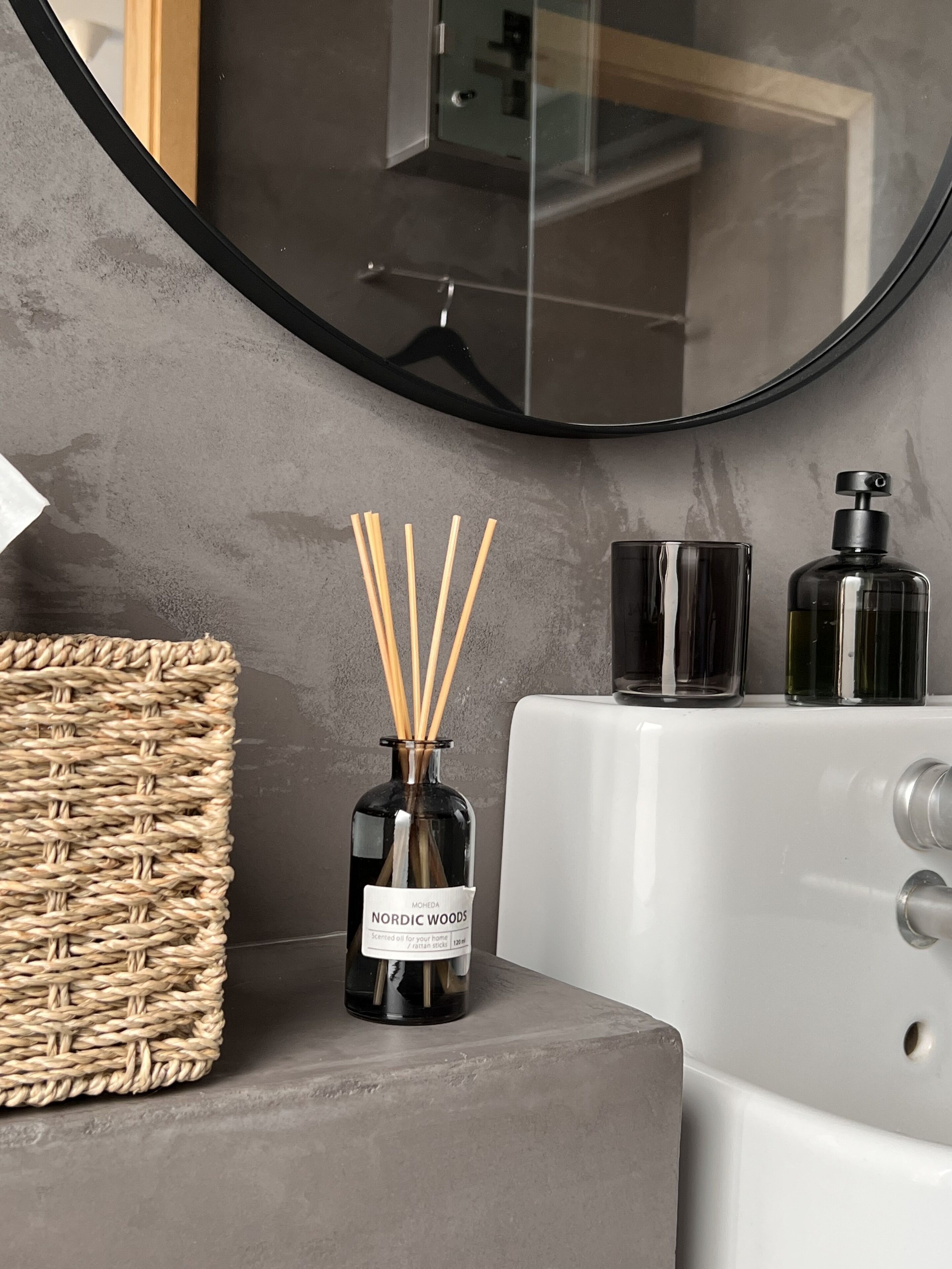 Un baño con un espejo redondo, un difusor de cañas y dos botellas de jabón líquido.