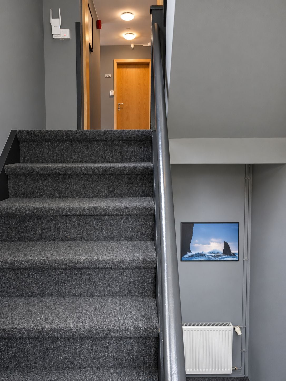 A staircase with carpeted steps and a metal handrail, leading to a room with a door and a wall-mounted picture.
