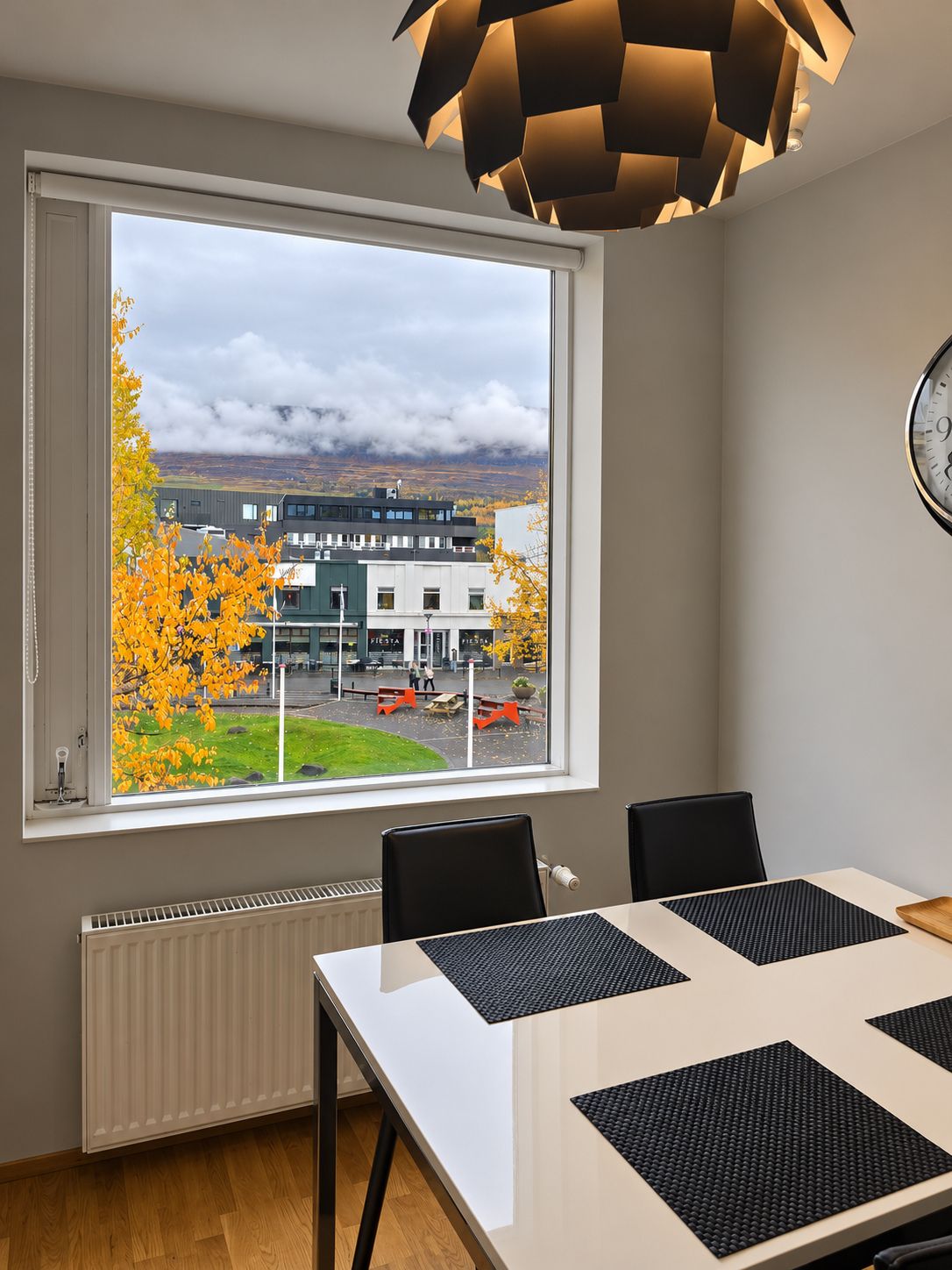 Une chambre moderne dotée d’une grande fenêtre, d’une table avec des sets de table noirs et d’un luminaire suspendu au design géométrique original.