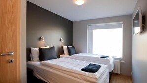 Une chambre d’hôtel moderne avec deux lits, une grande fenêtre et une porte.