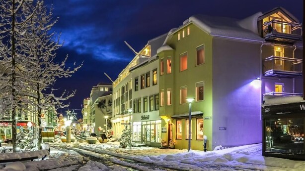 Une rue enneigée de nuit, avec des bâtiments, une devanture de magasin visible et des rails de tramway.