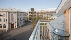 Une vue depuis un balcon donnant sur une rue bordée d’immeubles, notamment un immeuble blanc doté de fenêtres en arc de cercle et un immeuble moderne avec des balcons.