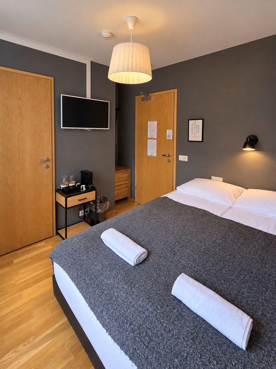Quarto de hotel com cama, escrivaninha com cafeteira, televisão e porta com aviso.