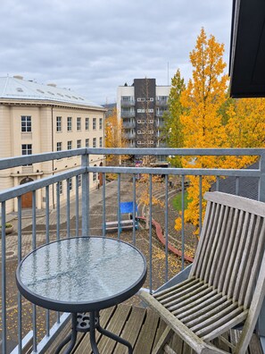 A balcony with a round table and a wooden chair, overlooking a cityscape with autumn-colored trees and buildings. - Torg Guest House (Akureyri)