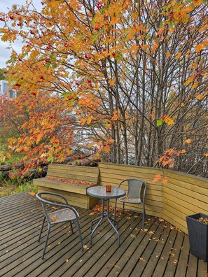 An outdoor seating area with a wooden bench and two chairs, surrounded by trees with autumn leaves. - Torg Guest House (Akureyri)