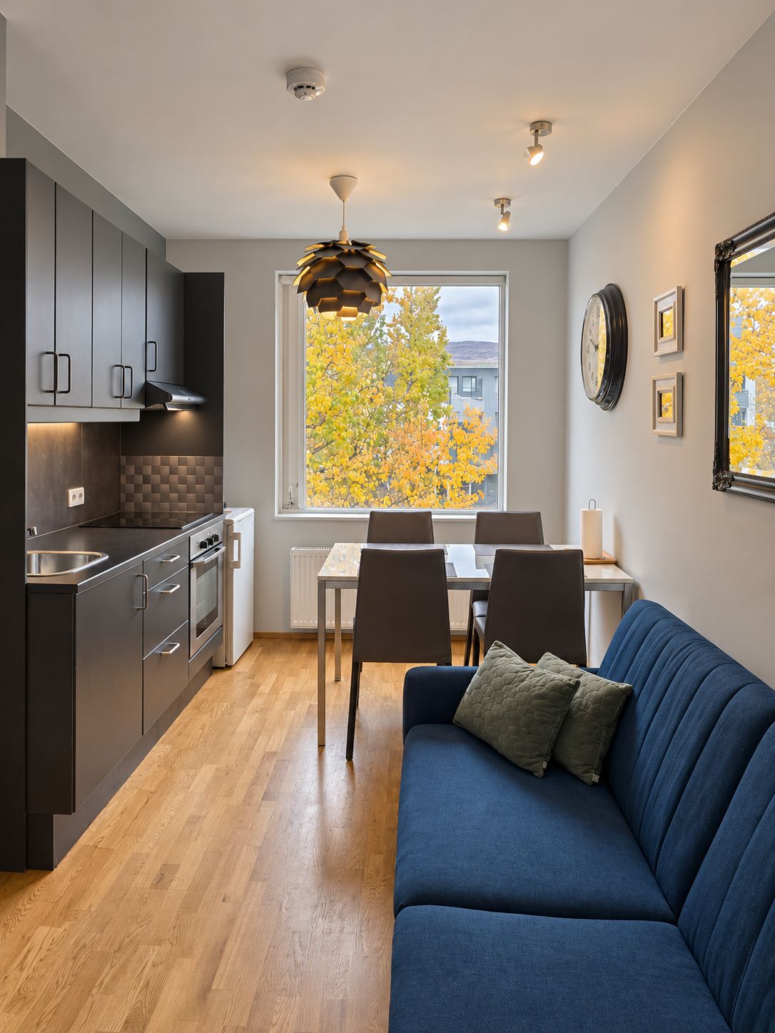 Una cocina moderna con armarios oscuros, un área de comedor con una mesa y sillas, y un sofá azul.