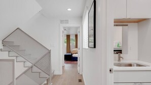 Un intérieur moderne comprenant un escalier, un couloir menant à une chambre et un espace cuisine.