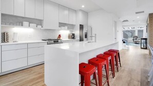 Une cuisine moderne avec des meubles blancs, un grand îlot central et des tabourets de bar rouges.