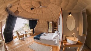 Une chambre confortable, aménagée comme une tente, avec un lit, une table de chevet et un grand miroir.