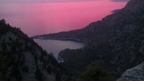 Un paysage côtier offrant une vue sur la mer et des îles lointaines, le tout sous un ciel rose.